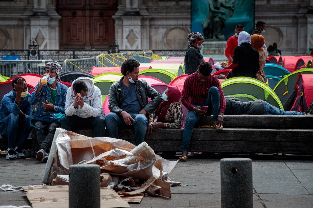 Des migrants sans-abri sont assis sur un banc à côté de tentes lors d'une action de l'association Utopia56 devant l'hôtel de ville de Paris