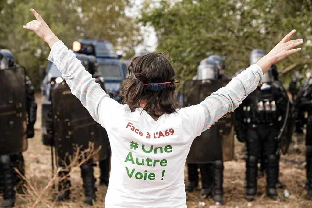 Image militant face aux forces de l’ordre, avec un t-shirt flaqué " Face à l'A69, une autre voie !"  